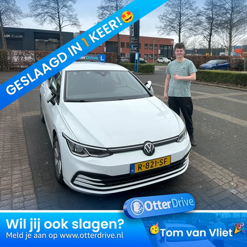 Man posing next to white Volkswagen car at dealership with Geslaagd in Keer! banner and OtterDrive logo